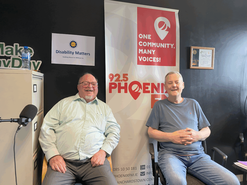 Two men seated and smiling in a radio studio. A "92.5 Phoenix FM" banner and "Disability Matters" sign are visible, conveying a friendly, inclusive setting.